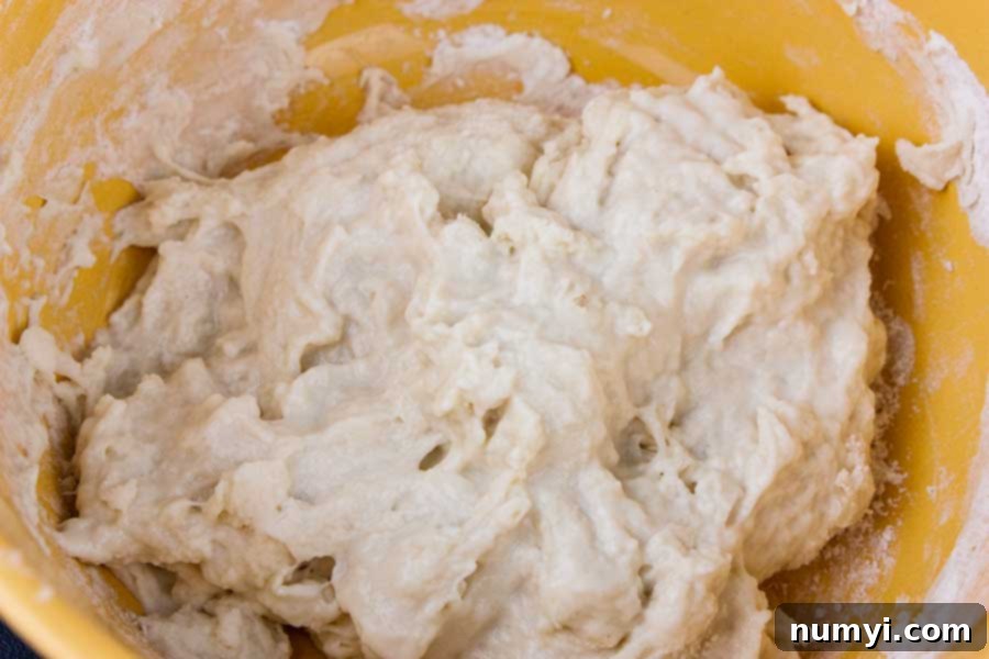 Simple Italian Christmas Panettone 4 Panettone starter ingredients mixed in a yellow bowl before rising, showing a wet, shaggy texture.
