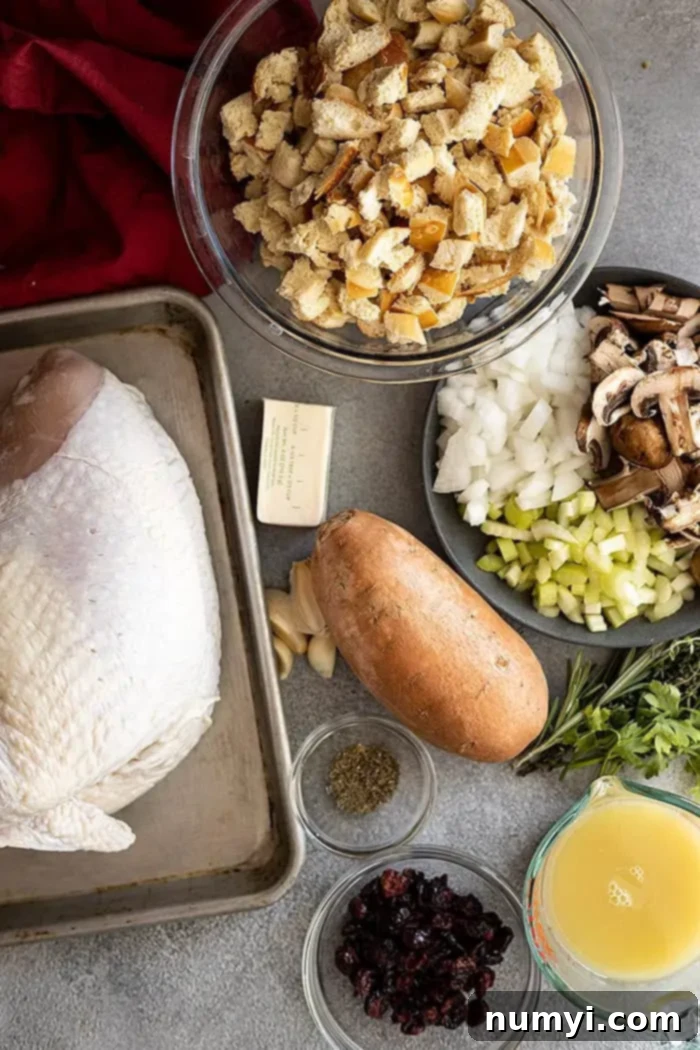 Sweet Potato Stuffed Turkey Roulade 3 Ingredients laid out on a wooden cutting board, including a loaf of bread, fresh herbs, sweet potatoes, cranberries, and a turkey breast, all ready to be assembled for the delicious Sweet Potato and Stuffing Turkey Roulade.