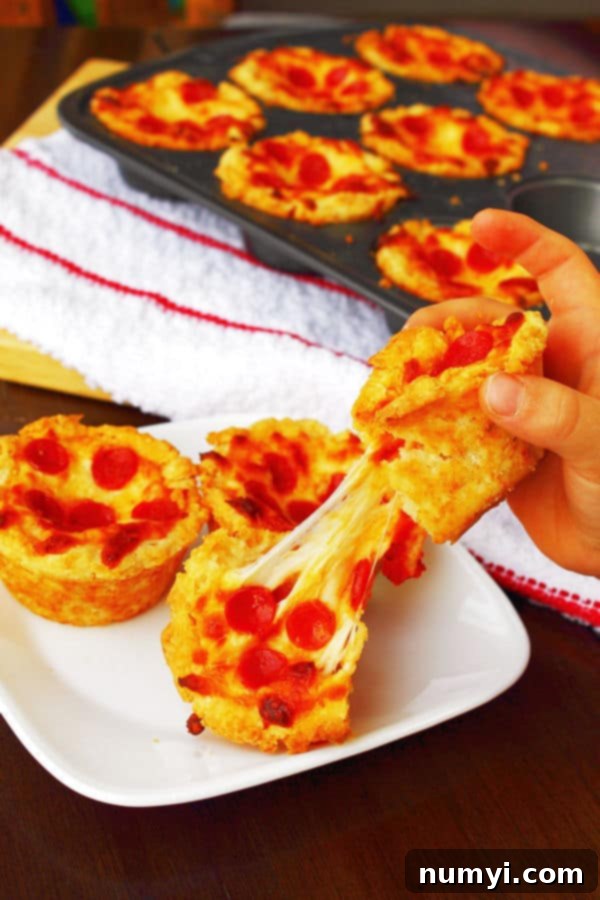 Mini Deep Dish Pizzas in a muffin tin in the background, and some on a white plate in the foreground with a hand pulling one of them apart with the cheese stretching from both halves, showing the melted cheese.