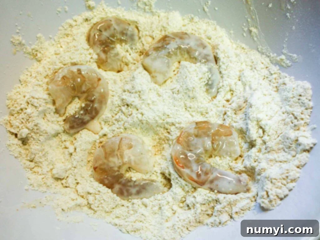 Raw shrimp being coated in a seasoned flour and cornmeal mixture.