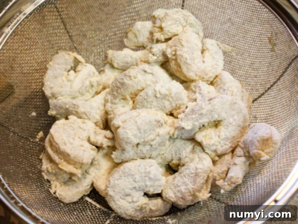 Freshly battered shrimp waiting to be fried, placed in a strainer.
