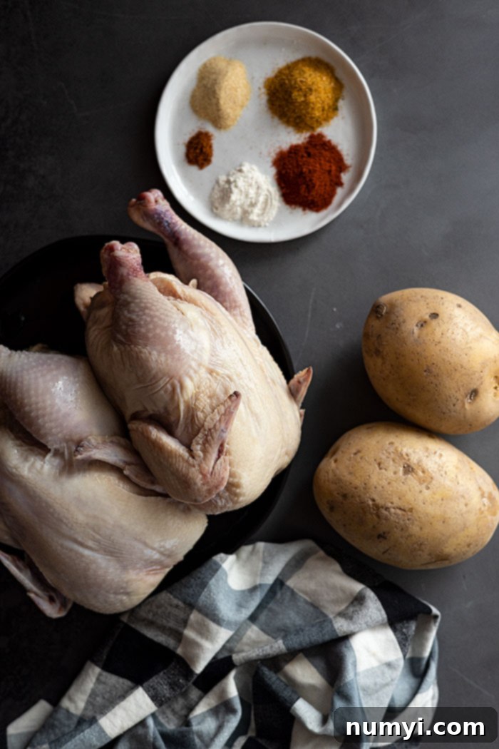 Overhead view of all the fresh ingredients laid out on a white surface, ready to prepare roasted cornish hens: two cornish hens, a bowl of cubed potatoes, a bowl of mixed spices, and a bottle of olive oil.