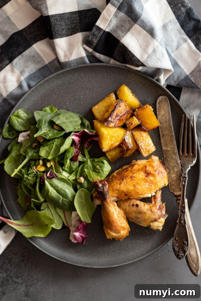 Overhead view of plated roasted cornish hen halves with crispy skin, served alongside golden roasted potatoes and a fresh green salad on a white plate, ready for a delicious meal.