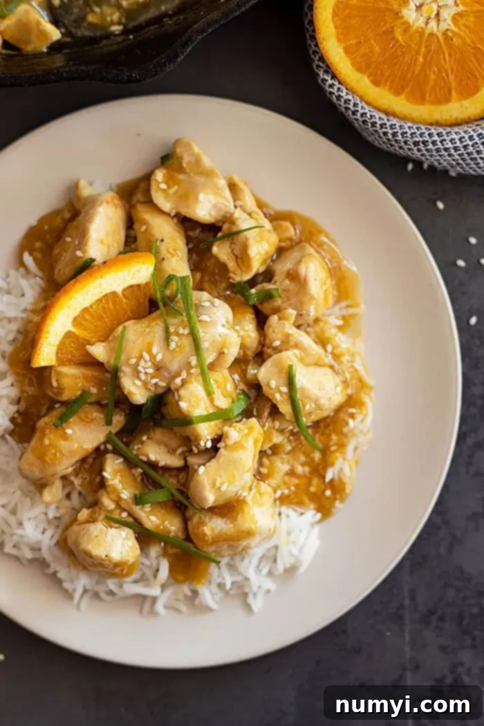 overhead: my easy orange chicken recipe on a bed of rice and garnished with green onions, sesame seeds, and orange slices