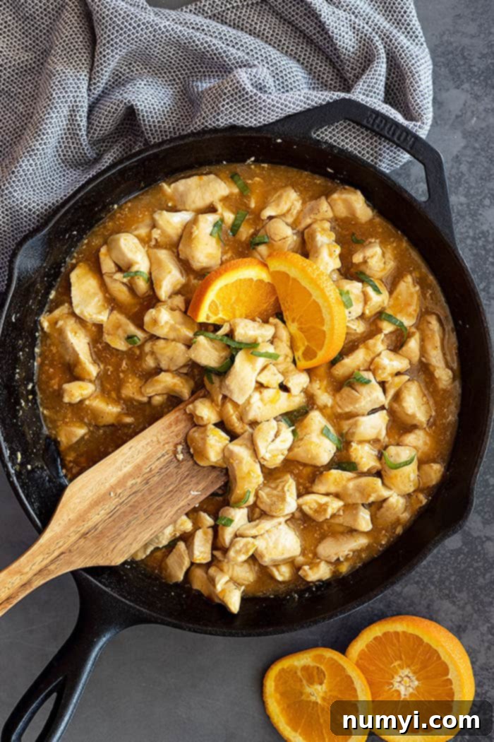 overhead: a wooden spoon stirring a skillet with orange sauce for orange chicken as well as cubed chicken pieces 