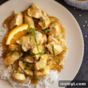 Overhead view of easy orange chicken on a bed of rice and garnished with green onions, sesame seeds, and orange slices.
