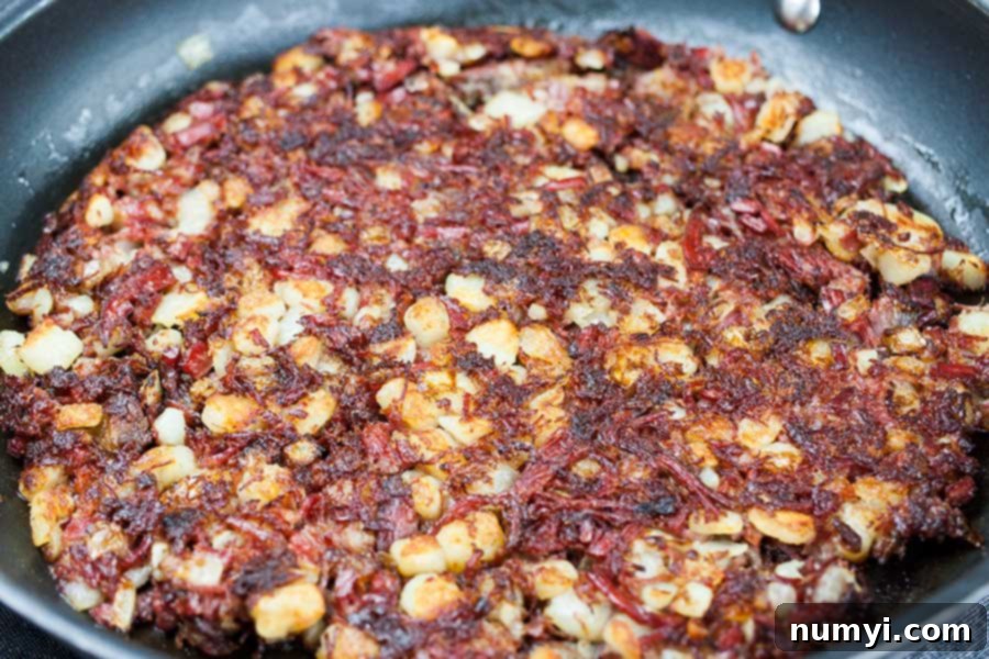 Close up of corned beef hash in a skillet, pressed down to form a crispy crust on the bottom.