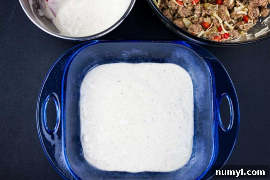Hearty Sausage Breakfast Casserole 3 The first layer of creamy batter spread at the bottom of a blue glass baking pan, ready for the sausage filling.