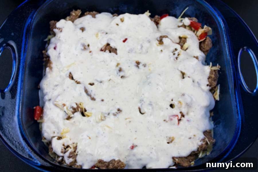Hearty Sausage Breakfast Casserole 4 An uncooked sausage breakfast cake, with layers of creamy batter and savory sausage filling clearly visible in a blue glass baking pan.