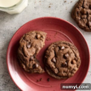 Cookies on a red plate with visible crumbs around and a glass of ice cold milk.