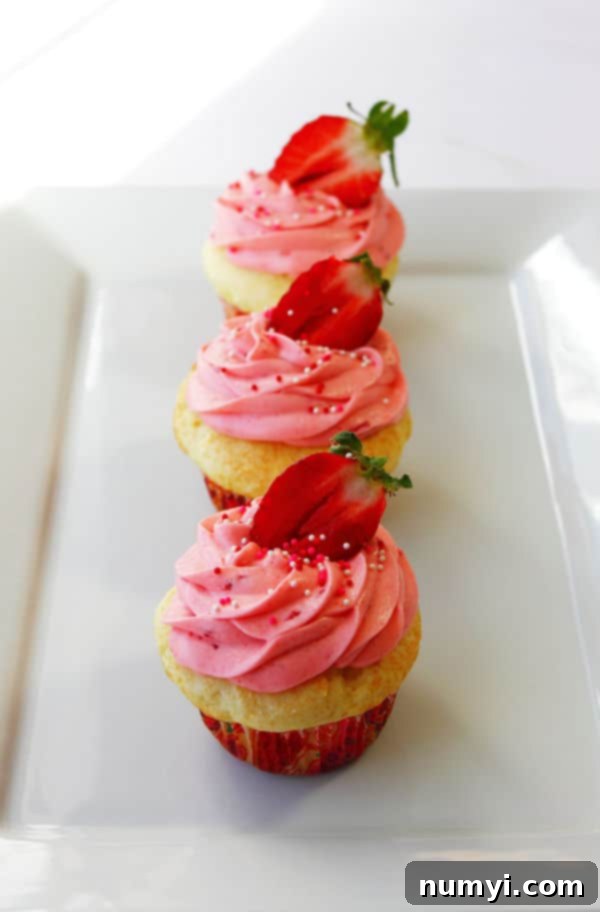 Little Strawberry Shortcakes 2 three Strawberry Shortcake Cupcakes in a line on a white serving platter with sprinkles and a halved strawberry on top