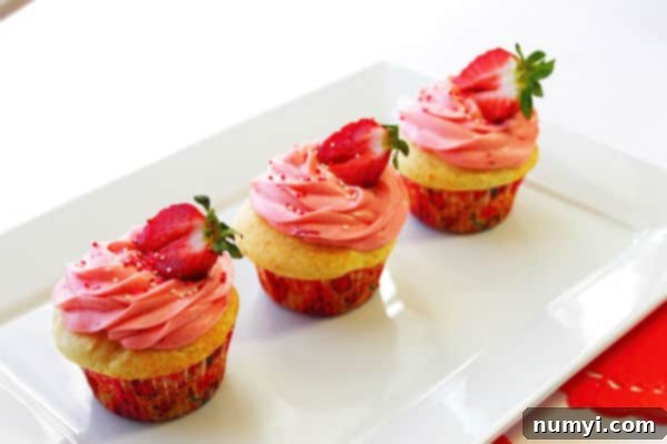 Little Strawberry Shortcakes 3 three strawberry shortcake cupcakes on a white platter with some pink frosting, sprinkles, and a strawberry garnish on top