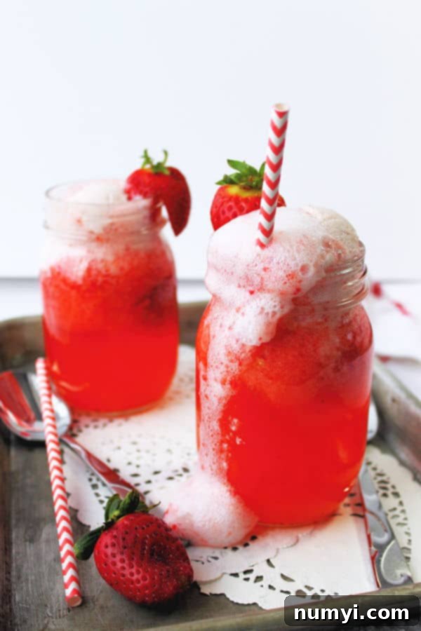Sparkling Strawberry Delight 2 Strawberry floats in mason jars, topped with a fresh sliced strawberry, and a red and white straw.