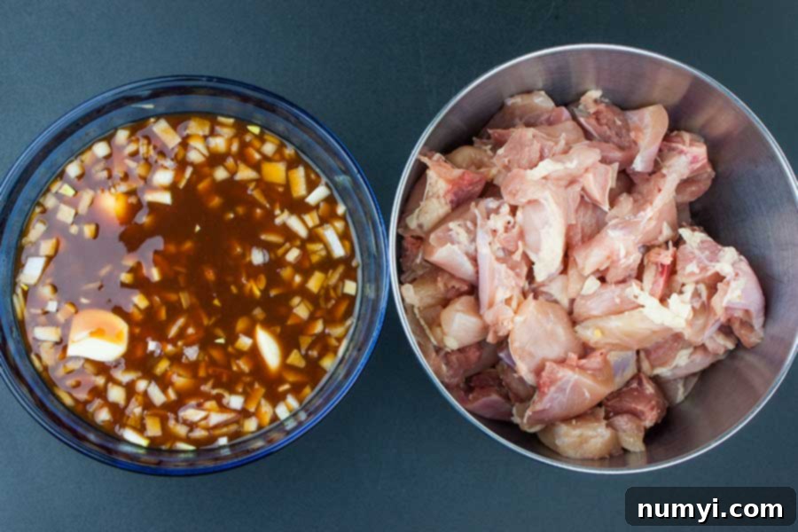 Cubed chicken pieces in a metal bowl beside a blue glass bowl of marinade ingredients.