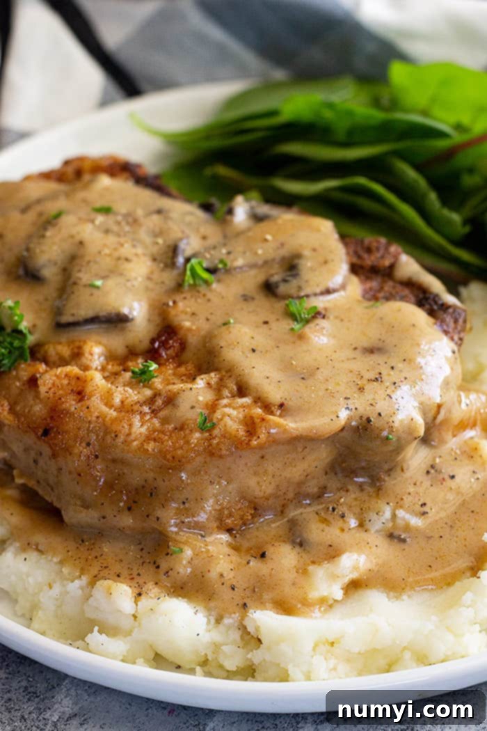 Close up of pork chop on a bed of mashed potatoes smothered in creamy mushroom gravy.