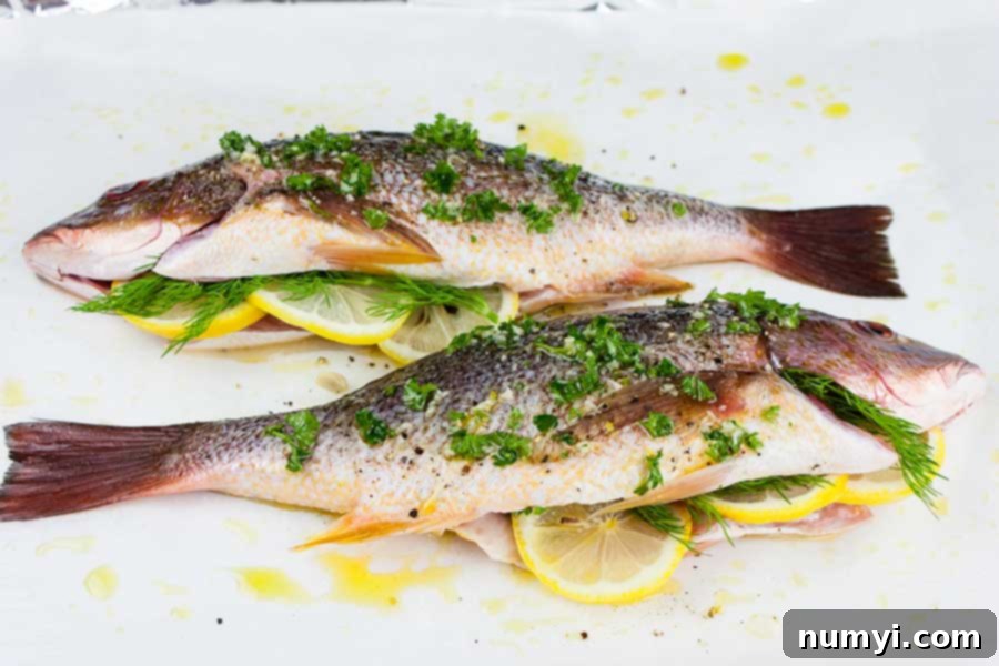 two whole red snappers prepped with herbs and seasonings on a parchment paper lined baking sheet
