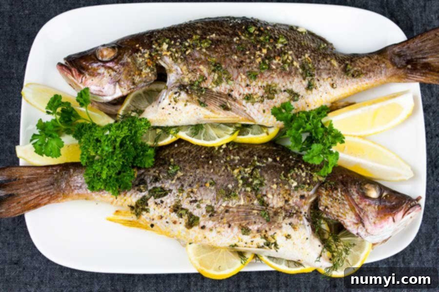 Baked Whole Red Snapper on a white platter garnished with lemon wedges and fresh parsley