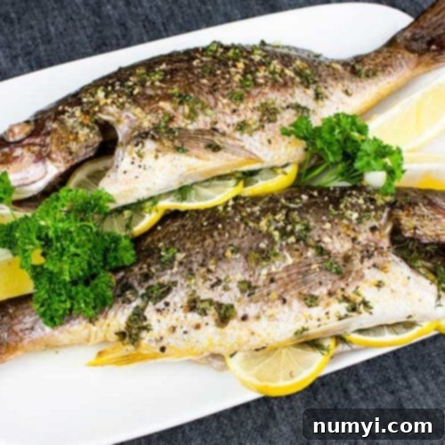 Baked whole red snapper on a white plate garnished with parsley.