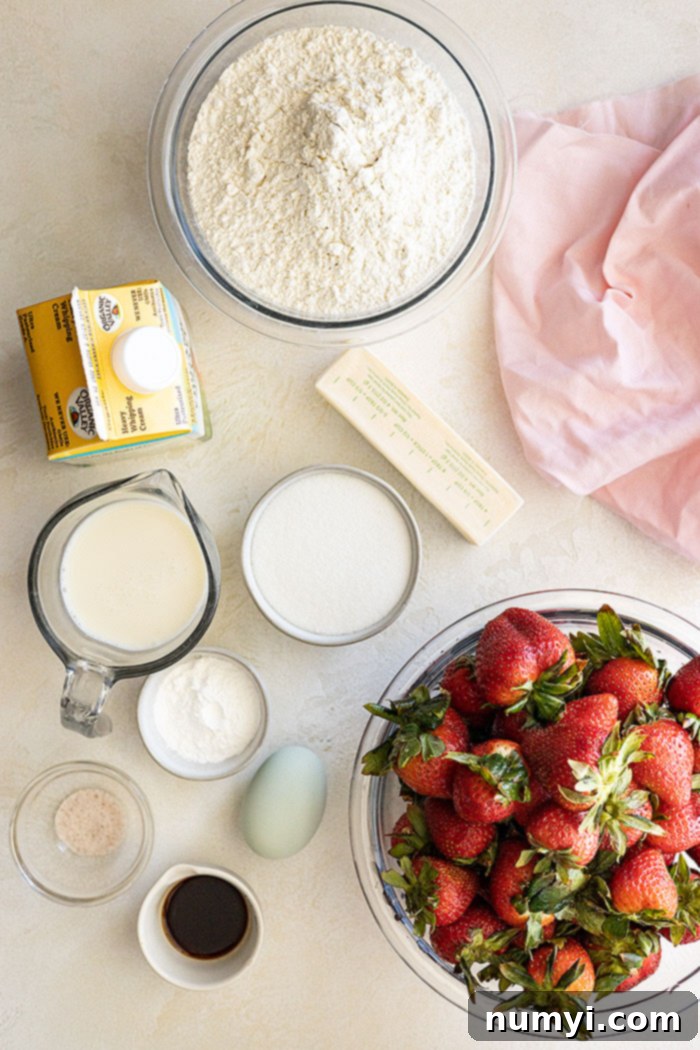 A flat lay shot displaying all the essential ingredients needed to make the homemade strawberry shortcake cake, including fresh strawberries, flour, butter, sugar, eggs, and heavy cream.