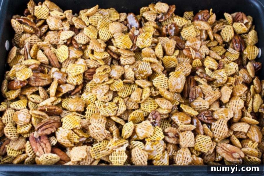 Praline Crunch Snack Mix baking in a roasting pan, with a golden brown caramel glaze.