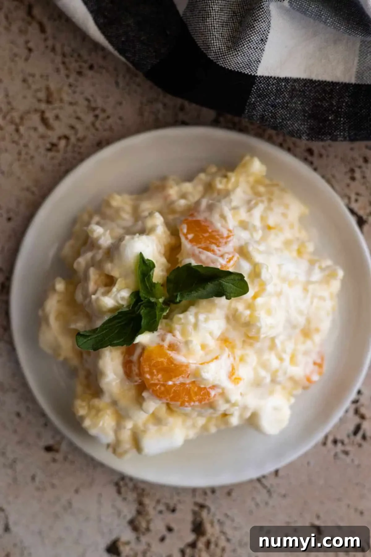 Golden Ambrosia Salad 2 Overhead view of frog eye salad on a white plate garnished with fresh mint.