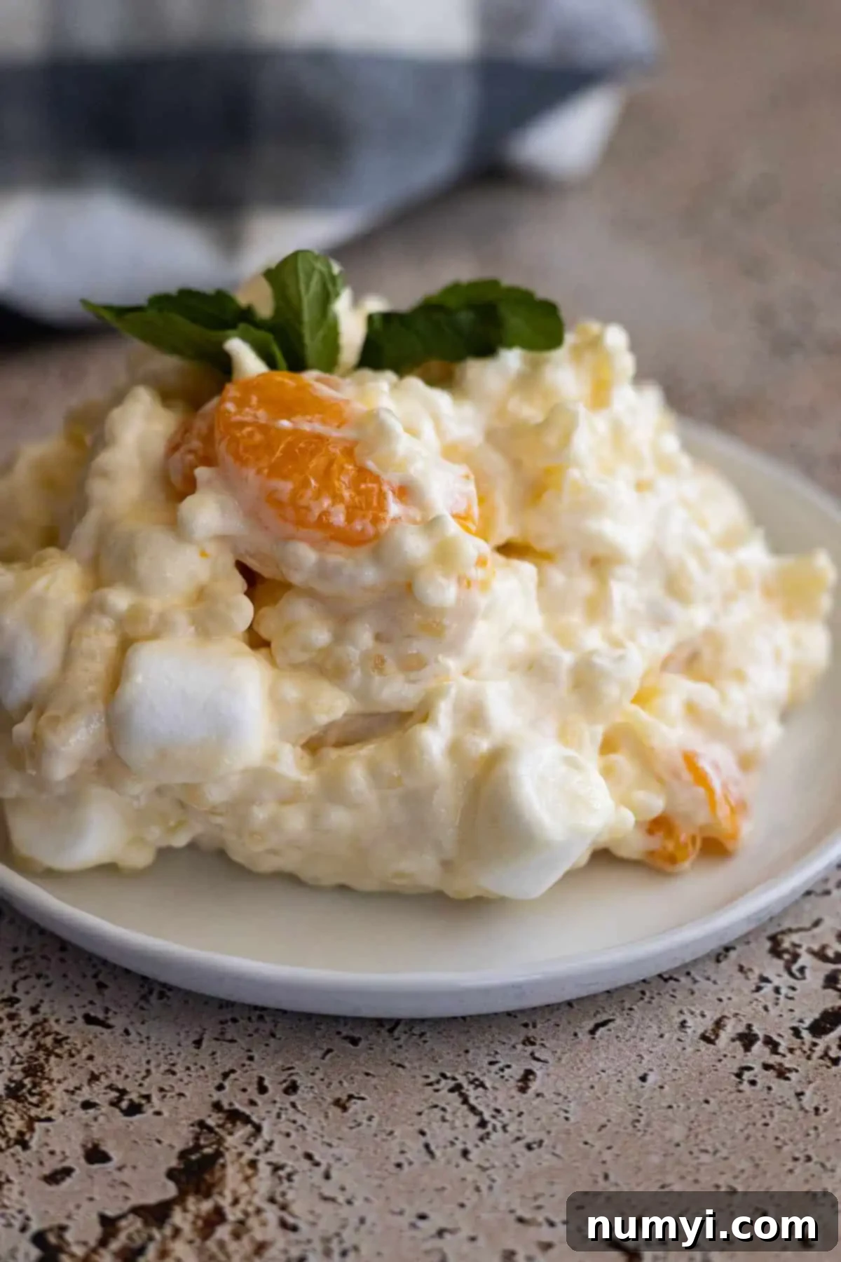 Golden Ambrosia Salad 6 Frog eye salad on a white plate with a blue napkin in the corner. Salad garnished with mint.