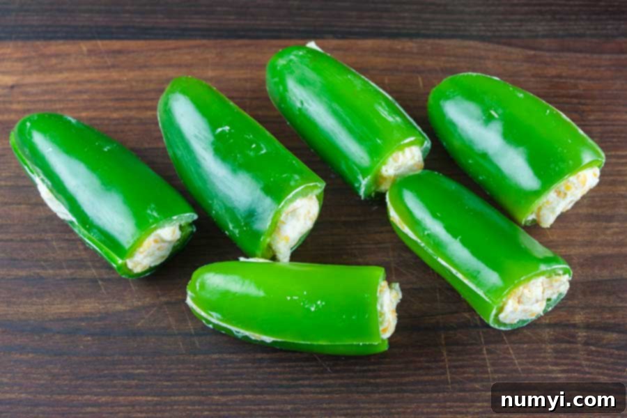 Ultimate Smoked Keto Armadillo Eggs 4 Jalapeno peppers stuffed with a creamy cheese mixture, ready to be wrapped in sausage.