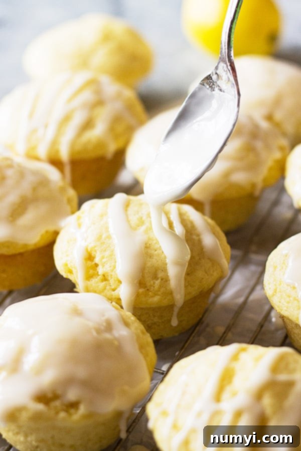 Drizzling homemade lemon glaze on freshly baked, light, and airy lemon muffins, ready for serving.