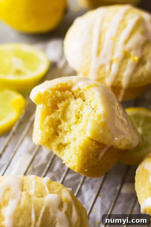 A close-up of a lemon muffin with a bite taken out, revealing its fluffy interior and a delicate lemon glaze.