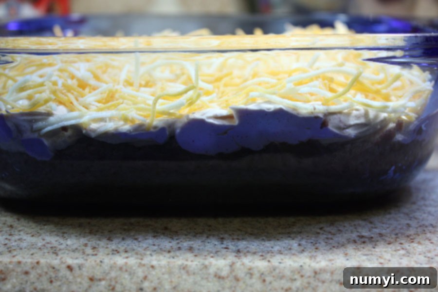 Black bean taco dip ingredients layered in a baking dish, showing the creamy mixture over the beans.