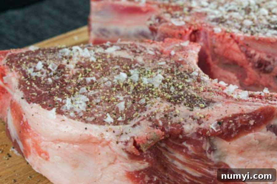 Raw bone-in pork chops seasoned with salt and pepper on a cutting board.