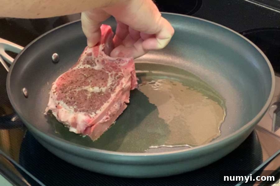 Thick cut bone-in pork chop being carefully placed into a hot frying pan.