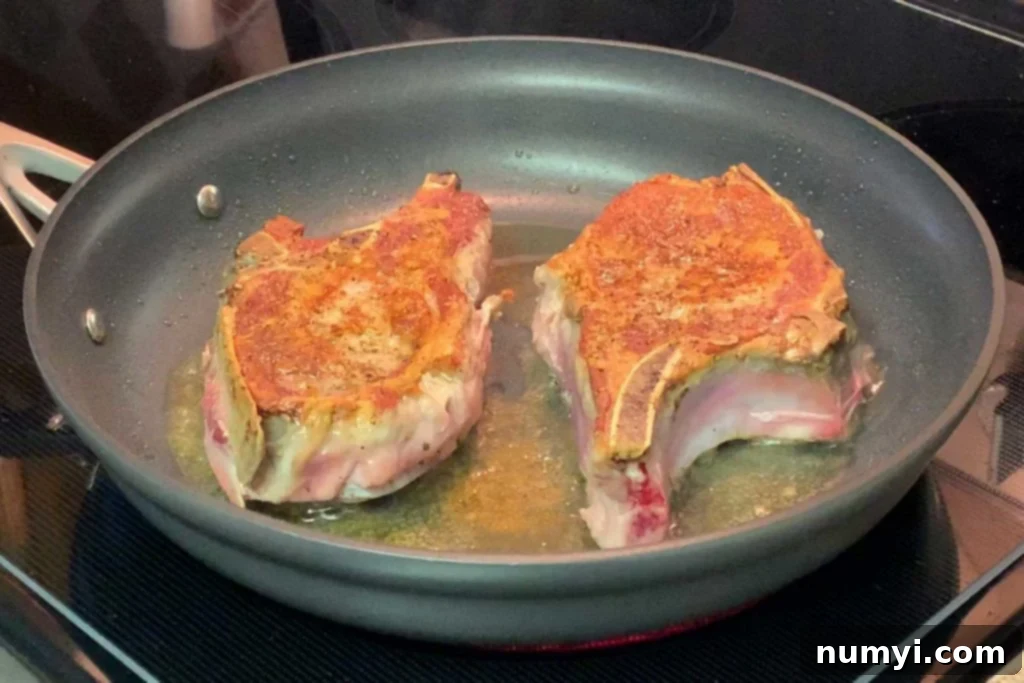 Pork chops cooking in a skillet, with one side perfectly caramelized.