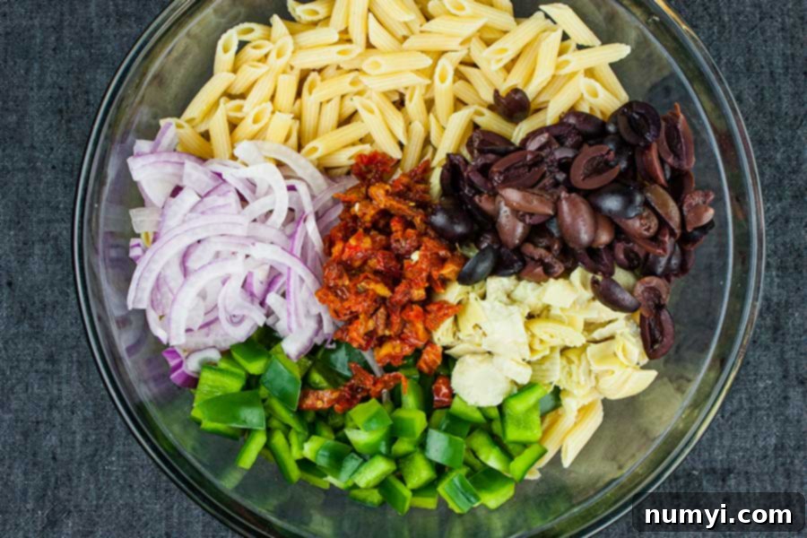 Zesty Greek Pasta Salad 3 Close-up of Greek Pasta Salad ingredients being mixed in a large bowl, highlighting the colorful components.