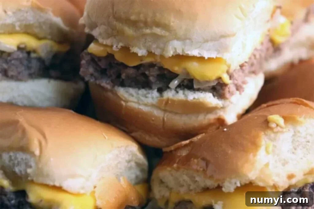 Ultimate Oven Cheeseburger Sliders 6 A close-up shot of perfectly assembled Oven Baked Sliders on a baking sheet, showing the soft buns, melted cheese, and juicy patty. The text overlay reads: 'Oven Baked Sliders - These taste just like Krystal's or White Castle hamburgers. Super easy to make!'