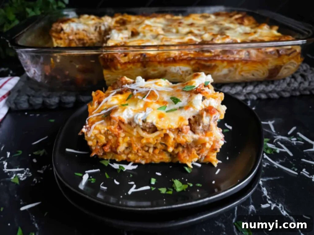 A serving of baked spaghetti garnished with parsley and Romano cheese on a dark plate on a dark surface.