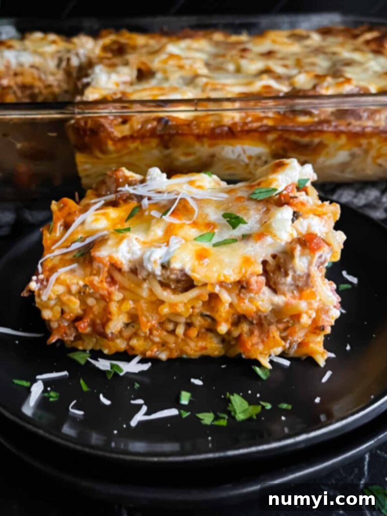 A serving of baked spaghetti garnished with parsley and Romano cheese on a dark plate on a dark surface.