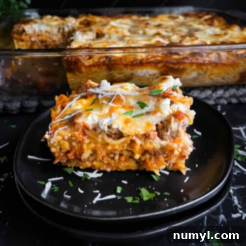 A serving of baked spaghetti garnished with parsley and Romano cheese on a dark plate on a dark surface.