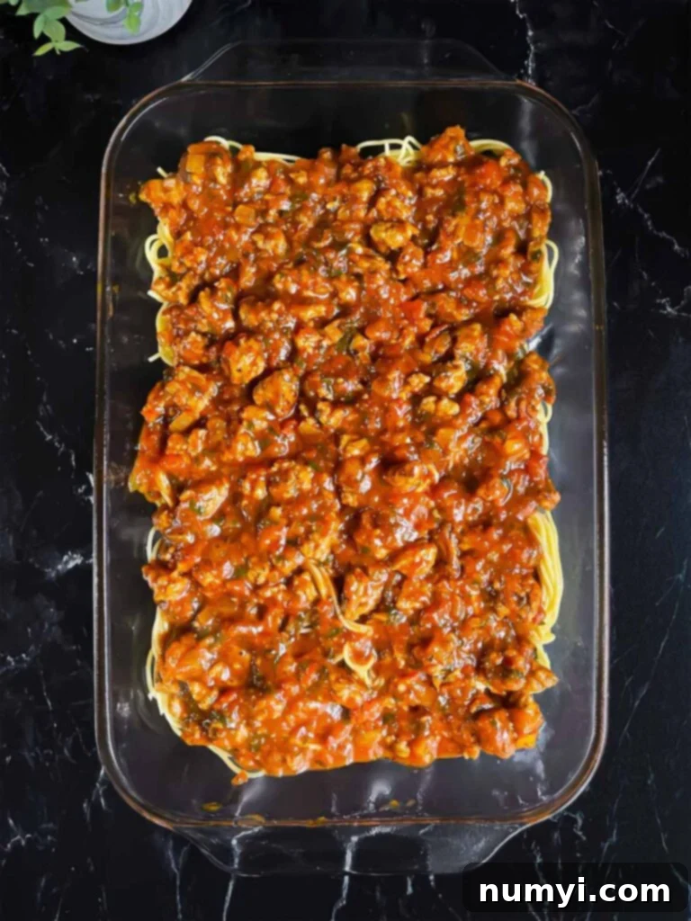 Layer of marinara sauce over the spaghetti in a glass baking pan.
