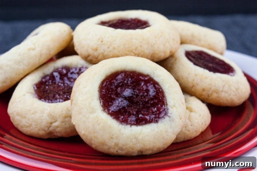 Homemade Jam Thumbprint Cookies 2 Stacked homemade Raspberry Thumbprint Cookies on a vibrant red plate, showcasing their golden edges and bright jam centers.