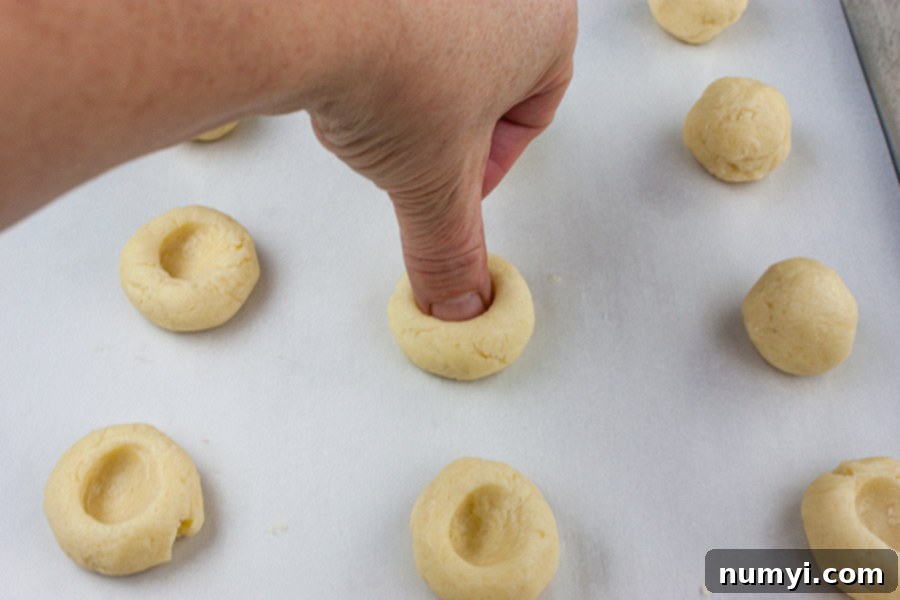 Homemade Jam Thumbprint Cookies 4 A hand gently pressing a thumb into a freshly rolled ball of cookie dough on a parchment-lined baking sheet to create the classic indentation.