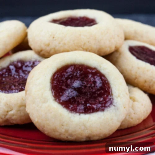 Homemade Jam Thumbprint Cookies 9 Thumbprint cookies stacked on a red plate.