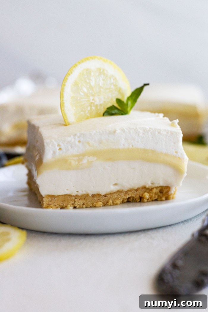 A piece of lemon dessert on a plate garnished with a lemon slice and mint. 