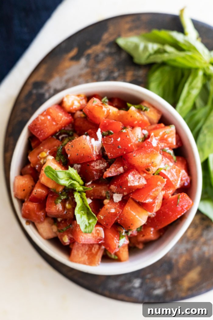 Bruschetta Made Simple 2 Overhead view of homemade bruschetta in a rustic bowl, garnished with a vibrant basil leaf and flakey sea salt. Fresh tomato basil bruschetta appetizer ready to serve.