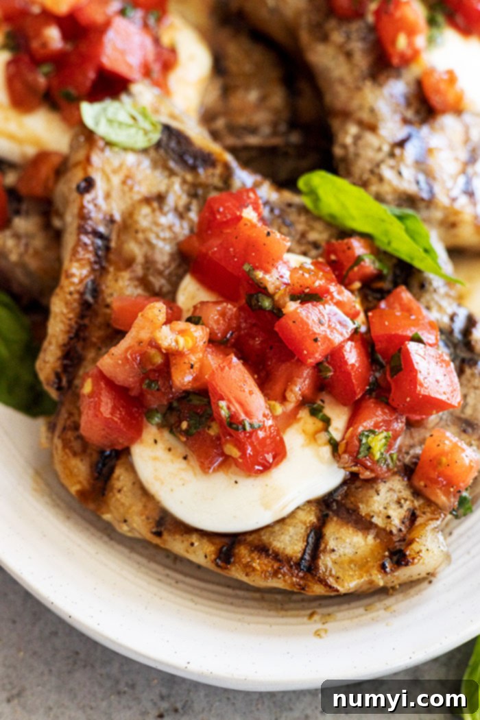 Flavorful Bruschetta Pork Chops 5 Close up of pork chop topped with melted mozzarella and bruschetta.