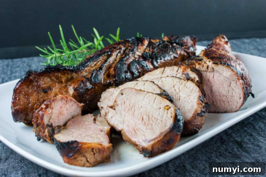 Your New Favorite Keto Grilled Pork Tenderloin 2 Keto grilled pork tenderloin sliced on a white platter garnished with fresh rosemary.