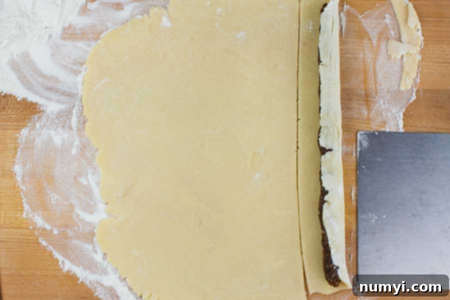A strip of cookie dough being rolled over a rope of fig filling, starting the cookie formation.