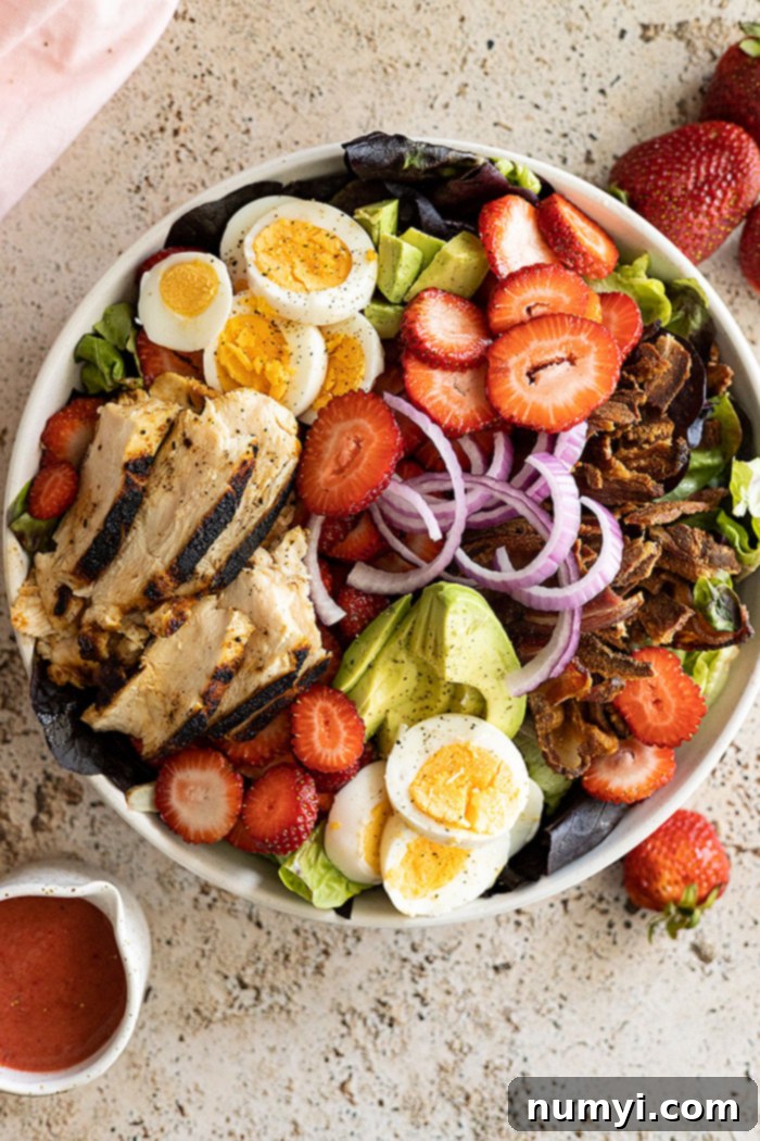 A vibrant Strawberry Cobb Salad generously topped with fresh strawberries, grilled chicken, bacon, hard-boiled eggs, and avocado, all drizzled with a homemade strawberry vinaigrette.