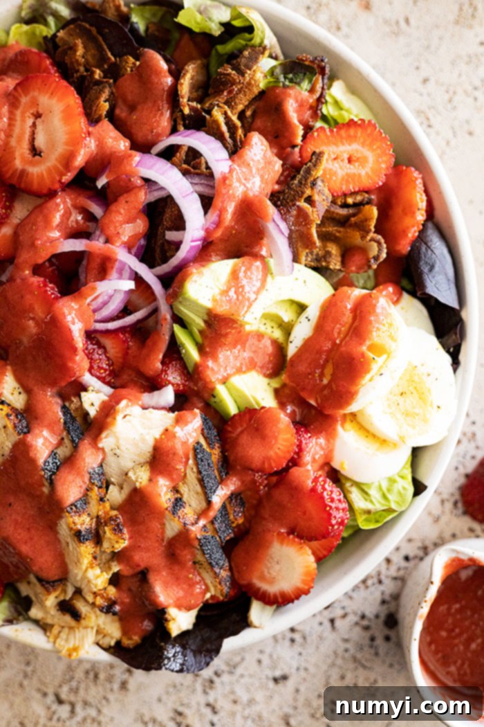 Close-up of a beautifully assembled Strawberry Cobb Salad, generously drizzled with the homemade strawberry vinaigrette, ready to be enjoyed.