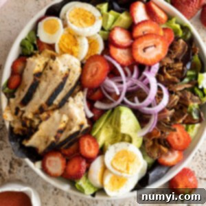 Overhead view of a large bowl of strawberry cobb salad with dressing off to the side.